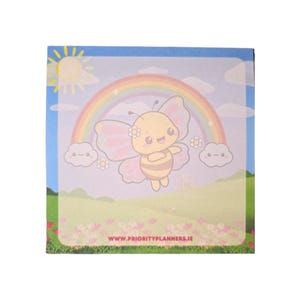 Może przedstawiać: Kwadratowy notatnik z kolorową ilustracją kreskówki pszczoły ze skrzydłami motyla, tęczą i słońcem. Tło przedstawia niebieskie niebo, chmury i zielone pole z kwiatami. Tekst "WWW.PRIORITYPLANNERS.IE" znajduje się na dole.