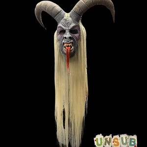 May include: A detailed mask of a horned demon with a menacing expression. The mask features gray skin, purple accents, and a long, red tongue. Long, light blonde hair flows from the mask. The text "UNSUB MASKS" is visible at the bottom.