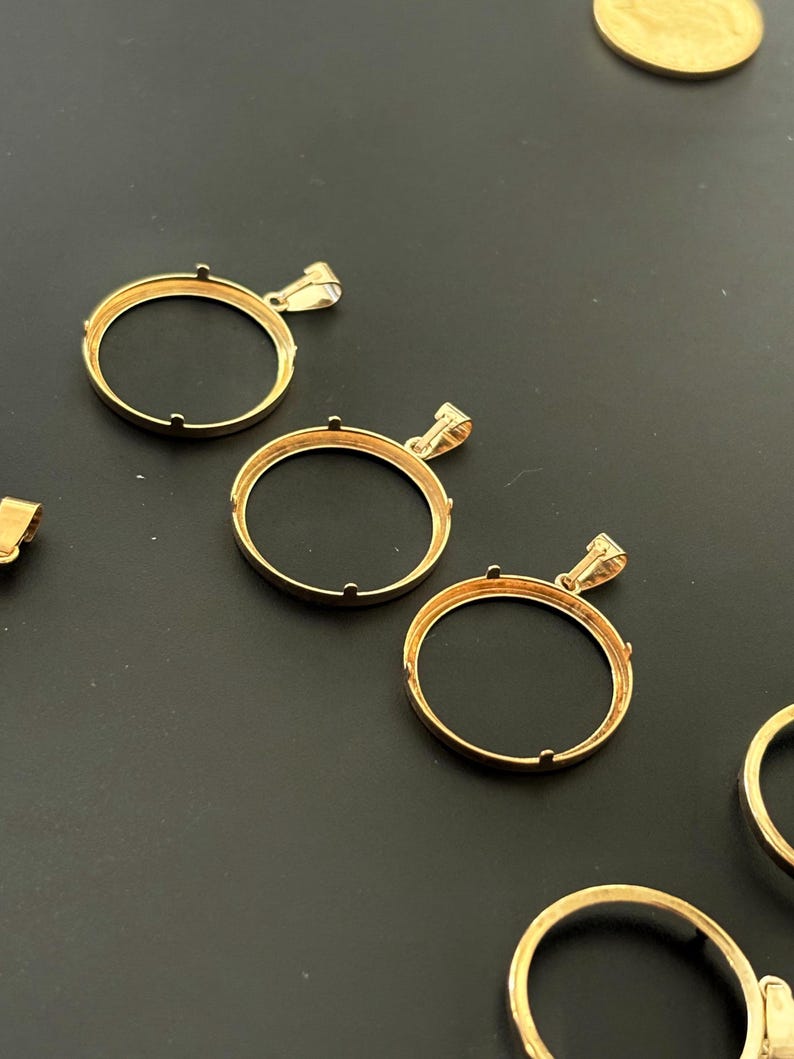 K&ouml;nnte beinhalten: Drei goldfarbene Metall-M&uuml;nzenanh&auml;nger-Bezel mit einer runden &Ouml;ffnung. Die Bezel haben eine glatte, polierte Oberfl&auml;che und sind so konzipiert, dass sie eine M&uuml;nze oder ein anderes rundes Objekt aufnehmen k&ouml;nnen.