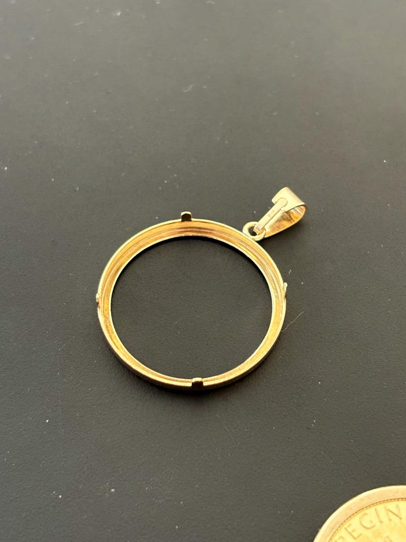 K&ouml;nnte beinhalten: Goldfarbener Anh&auml;nger mit einem runden Rahmen und einer kleinen Schlaufe oben. Der Rahmen ist f&uuml;r eine M&uuml;nze oder ein Medaillon ausgelegt.
