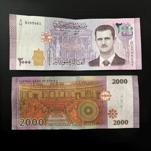 Op de afbeelding: Een Syrisch bankbiljet van 2000 pond met een portret van Bashar al-Assad op de voorkant en een uitzicht op het Syrische parlementsgebouw op de achterkant. Het bankbiljet is in goede staat en heeft serienummer 8399461.