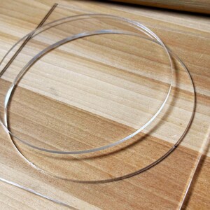 May include: Clear, thin, circular plastic pieces, possibly for crafting or jewelry making, are arranged on a light brown wooden surface. The plastic appears transparent, with a slight sheen, and is curved into circles.