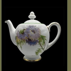 May include: A white tea set with a floral design featuring purple flowers and green leaves. The set includes a teapot, creamer, sugar bowl, cup and saucer, and a bowl with a saucer.