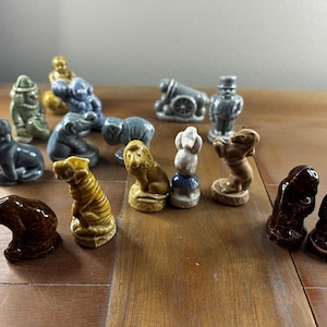 May include: A collection of 15 miniature ceramic figurines, including a lion, a tiger, a monkey, a dog, a cat, a clown, a man in a top hat, and a cannon. The figurines are painted in various shades of brown, gray, and yellow.