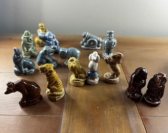May include: A collection of 15 miniature ceramic figurines, including a lion, a tiger, a monkey, a dog, a cat, a clown, a man in a top hat, and a cannon. The figurines are painted in various shades of brown, gray, and yellow.