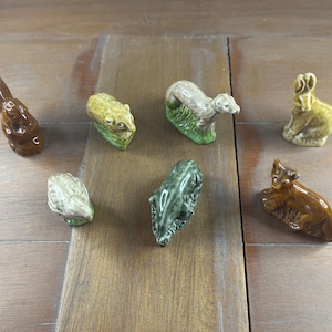 Puede incluir: Una colección de siete pequeñas figuritas de animales de cerámica. Las figuritas están pintadas en varios tonos de marrón, verde y blanco. Los animales incluyen una ardilla, un tejón, una rana, un conejo, una comadreja, un erizo y un oso.