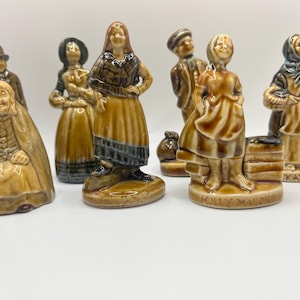 Puede incluir: Conjunto de diez figuritas de cerámica que representan a varios personajes con ropa tradicional irlandesa. Las figuritas están pintadas a mano en marrón, blanco y negro con detalles intrincados. Cada figurita tiene un nombre único impreso en la base, incluyendo "Molly Malone" y "Kathleen".