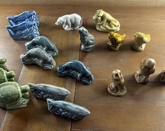 Può includere: Una collezione di piccole statuette di animali in ceramica che include tartarughe verdi, pesci blu, un orso bianco, una scimmia color cuoio, una rana grigia, uccelli gialli, un gufo marrone e figure sedute color cuoio. Finitura lucida.