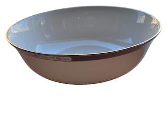 May include: A white ceramic bowl with a gold rim and a decorative band featuring a floral pattern in red and gold. The bowl has a slightly angled design, suitable for serving or display.
