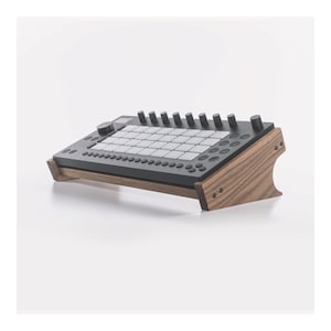 May include: A wooden stand for a music keyboard with a dark gray surface and black knobs. The stand is made of light brown wood with a natural grain pattern.