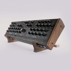 May include: A black synthesizer with numerous knobs and buttons, mounted on a wooden stand. The synthesizer has the word "ENVELOPES" printed on it. The stand is made of dark wood and is angled for optimal use.