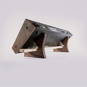 May include: A wooden stand with a dark walnut finish supports a black electronic device. The stand has a curved design with a light-colored wood support. The device has the text "REVERENTIAL TAKES" printed on it.