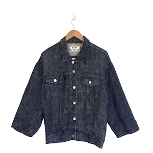 Puede incluir: Una chaqueta vaquera azul oscuro con cierre de botones y una etiqueta blanca que dice "Acne Studios".