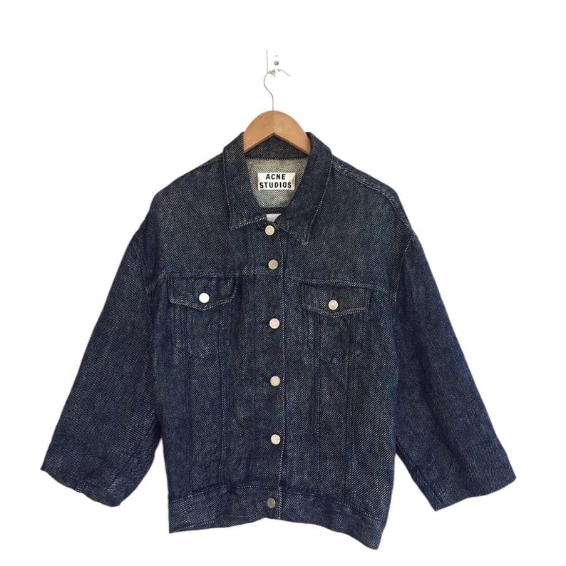 Puede incluir: Una chaqueta vaquera azul oscuro con cierre de botones y una etiqueta blanca que dice "Acne Studios".