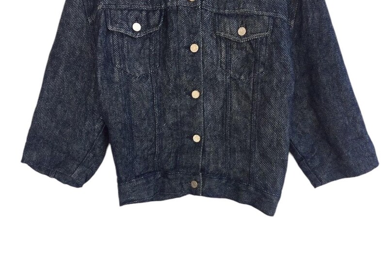 Puede incluir: Una chaqueta vaquera azul oscuro con cierre de botones y dos bolsillos en el pecho. La chaqueta tiene una longitud ligeramente recortada y un estilo cl&aacute;sico.