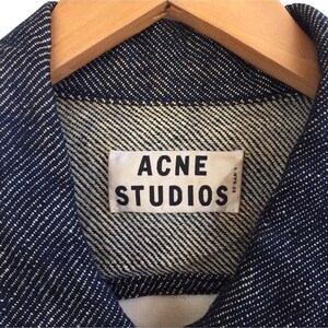 Puede incluir: Primer plano de una chaqueta vaquera azul con una etiqueta blanca que dice "Acne Studios" en letras negras.