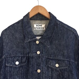 Puede incluir: Una chaqueta vaquera azul oscuro con cierre de botones y una etiqueta blanca que dice "Acne Studios".
