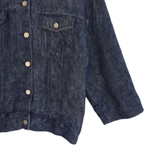 Puede incluir: Una chaqueta vaquera azul oscuro con cierre de botones y un solo bolsillo en el pecho. La chaqueta tiene un corte ligeramente holgado y una tela texturizada.