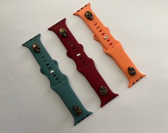 May include: Three silicone watch bands with skull accents. The bands are in teal, burgundy, and peach.