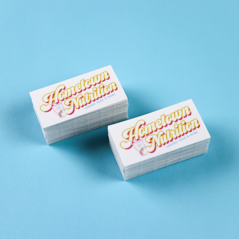 May include: Two stacks of white business cards with the text "Hometown Nutrition" in yellow and pink lettering. The text "Loaded Teas & More" is in smaller black lettering below the main text.