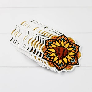 K&ouml;nnte beinhalten: Ein Stapel bunter Elefanten-Mandala-Aufkleber. Das Mandala ist ein kreisf&ouml;rmiges Design mit einem Elefantenkopf in der Mitte. Der Elefant ist braun mit einem gelben Sonnenblumenmuster drumherum. Das Mandala ist von einem schwarzen Umriss umgeben.
