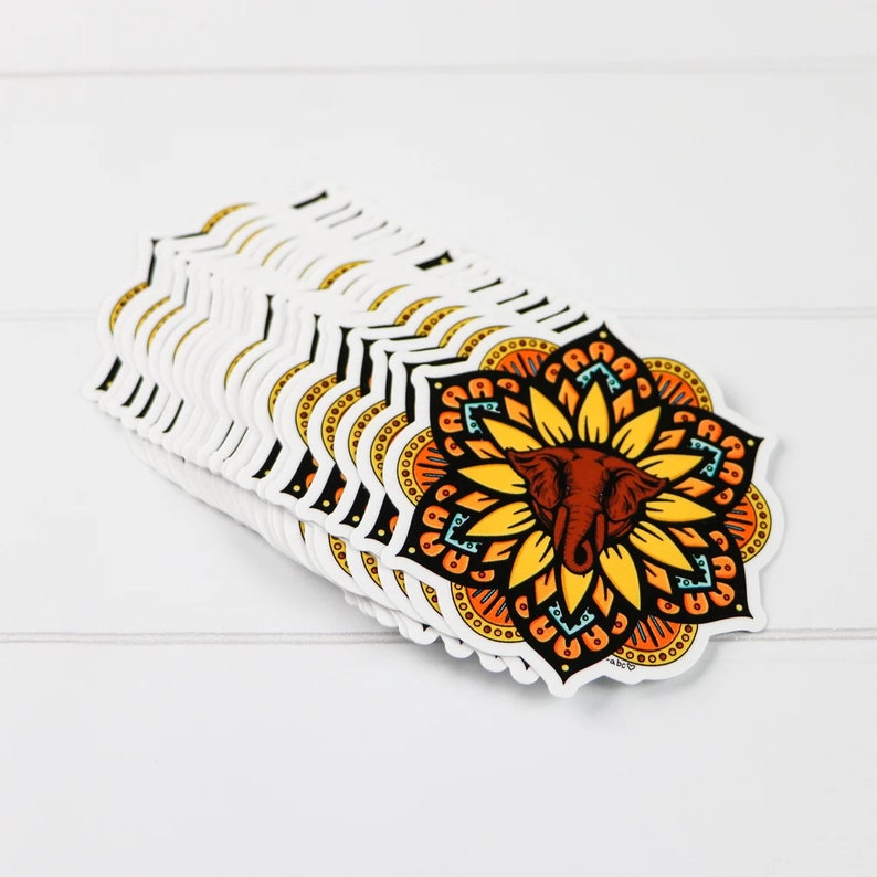 K&ouml;nnte beinhalten: Ein Stapel bunter Elefanten-Mandala-Aufkleber. Das Mandala ist ein kreisf&ouml;rmiges Design mit einem Elefantenkopf in der Mitte. Der Elefant ist braun mit einem gelben Sonnenblumenmuster drumherum. Das Mandala ist von einem schwarzen Umriss umgeben.