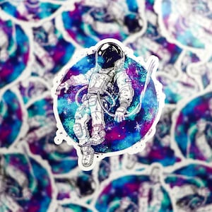 K&ouml;nnte beinhalten: Eine Schwarzwei&szlig;illustration eines Astronauten, der im Weltraum schwebt. Der Astronaut tr&auml;gt einen Raumanzug und einen Helm. Der Hintergrund ist ein Aquarellbild einer Galaxie in Blaut&ouml;nen, Lila und Rosa.