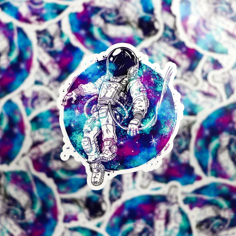 K&ouml;nnte beinhalten: Eine Schwarzwei&szlig;illustration eines Astronauten, der im Weltraum schwebt. Der Astronaut tr&auml;gt einen Raumanzug und einen Helm. Der Hintergrund ist ein Aquarellbild einer Galaxie in Blaut&ouml;nen, Lila und Rosa.