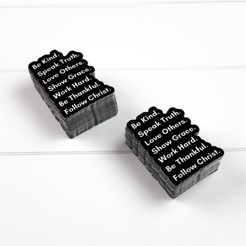 May include: A stack of black square stickers with white text that reads "Be Kind. Speak Truth. Love Others. Show Grace. Work Hard. Be Thankful. Follow Christ."