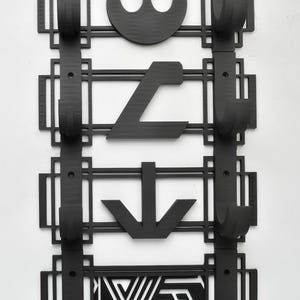 May include: Black wall-mounted coat rack with four hooks. Each hook is decorated with a different Star Wars symbol: the Rebel Alliance symbol, the Imperial symbol, a downward arrow, and a geometric pattern.