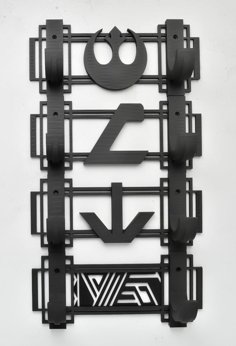May include: Black wall-mounted coat rack with four hooks. Each hook is decorated with a different Star Wars symbol: the Rebel Alliance symbol, the Imperial symbol, a downward arrow, and a geometric pattern.