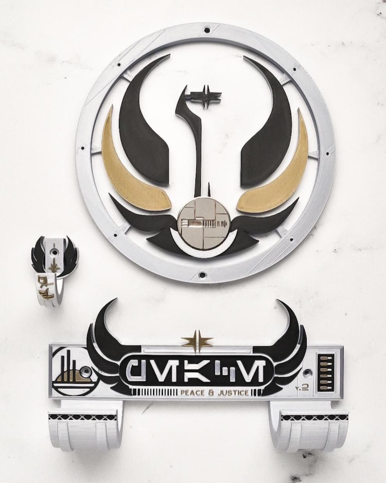 May include: A set of three-dimensional wall art pieces featuring a circular emblem, a small ring, and a rectangular sign. The emblem has black, gold, and silver elements. The sign reads "CIVIK'M PEACE & JUSTICE" in black and white.
