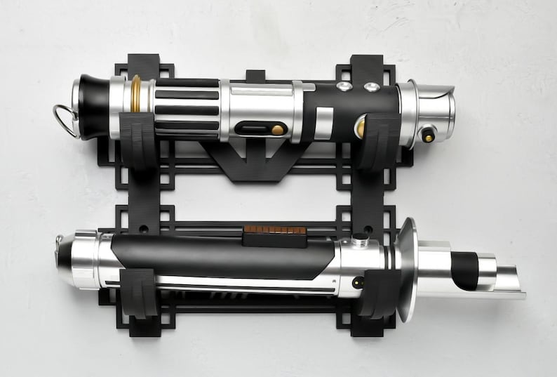 May include: A black metal wall mount with two lightsaber holders. The lightsabers are silver, black, and gold.