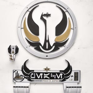 May include: A set of three-dimensional wall art pieces. The largest piece is a circular emblem with black, gold, and silver accents. Below is a rectangular piece with the text "CMKM PEACE & JUSTICE". A smaller ring-shaped piece is also included.