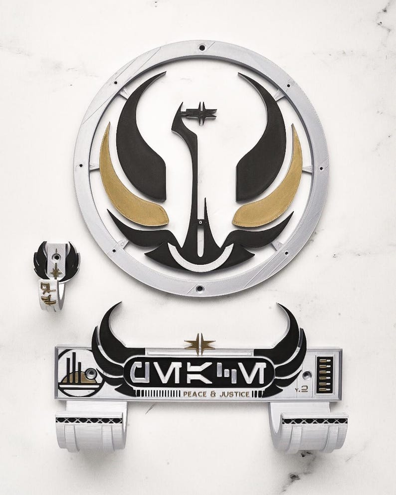 May include: A set of three-dimensional wall art pieces. The largest piece is a circular emblem with black, gold, and silver accents. Below is a rectangular piece with the text "CMKM PEACE & JUSTICE". A smaller ring-shaped piece is also included.