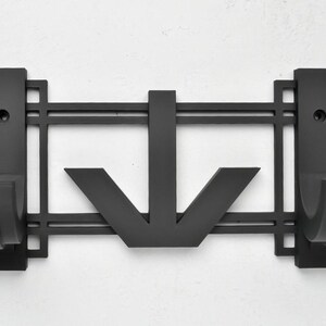 May include: Black metal wall mounted coat rack with an art deco design. The rack has two hooks and a downward pointing arrow in the center.