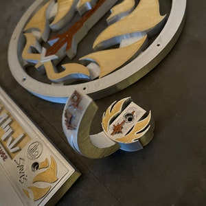以下が含まれることがあります： スタイリッシュなデザインの銀と金の金属製の壁掛けフック。フックは、円形のベースを持つ湾曲した腕の形をしています。ベースには、星と炎のスタイリッシュなデザインが施されています。