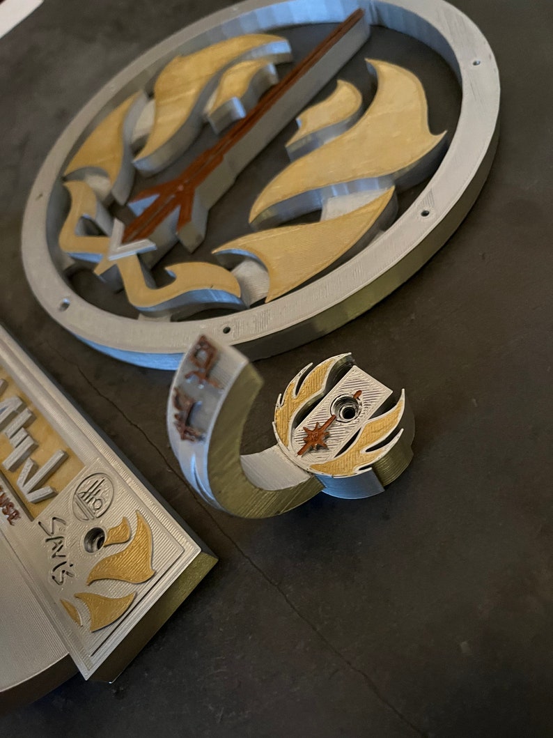 以下が含まれることがあります： スタイリッシュなデザインの銀と金の金属製の壁掛けフック。フックは、円形のベースを持つ湾曲した腕の形をしています。ベースには、星と炎のスタイリッシュなデザインが施されています。