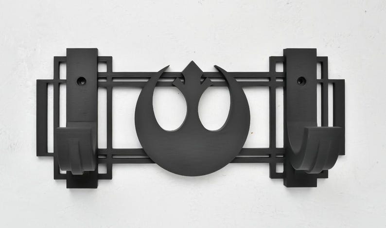 May include: Black metal wall mount with two hooks and a Rebel Alliance symbol in the center. The hooks are designed to hold lightsabers.