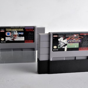May include: Two gray video game cartridges, one labeled "Tecmo Super Bowl" with a football player graphic, and the other "Major League Baseball" with a baseball player graphic. The cartridges are in black and gray holders.