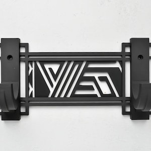 May include: Black metal wall hook with a geometric design. The hook has two hooks and a rectangular shape.