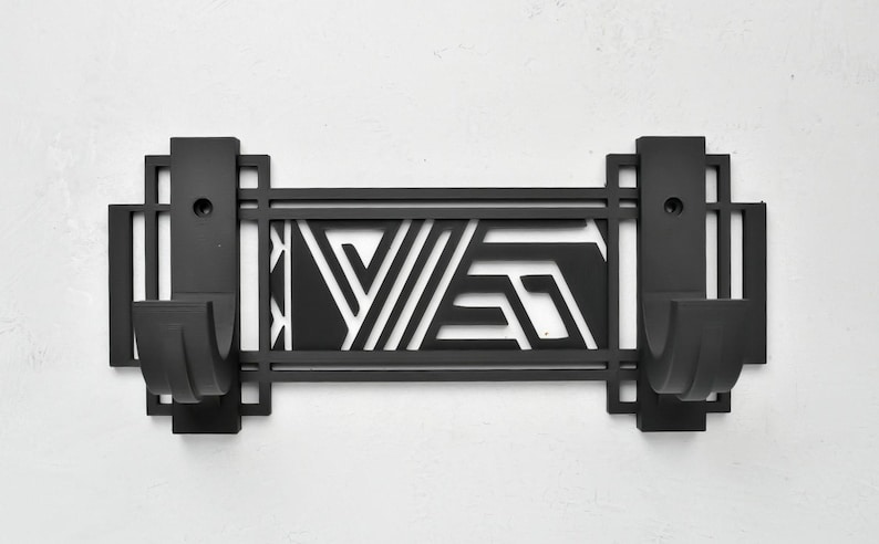 May include: Black metal wall hook with a geometric design. The hook has two hooks and a rectangular shape.