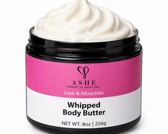 Pode incluir: Um frasco de manteiga corporal batida com tampa e base pretas. O frasco tem um rótulo rosa e branco com o texto "ASHÉ Spiritual Skincare Love & Attraction" e "Whipped Body Butter". O frasco contém 226g de produto.