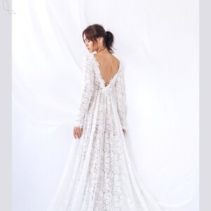 May include: A white lace wedding dress with long sleeves and a low back. The dress has a flowing skirt and a fitted bodice.