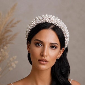 May include: A wide, padded headband completely covered in small, round, white faux pearls of varying sizes. The accessory features a dense, textured surface created by the clustered arrangement of the pearls, providing a full and rounded profile.