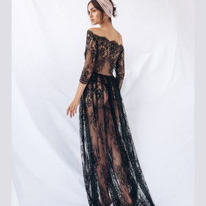 May include: A black lace maxi dress with a sheer, flowing skirt and an off-the-shoulder neckline. The dress is worn by a model with a pink headband.