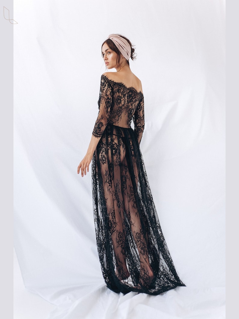 May include: A black lace maxi dress with a sheer, flowing skirt and an off-the-shoulder neckline. The dress is worn by a model with a pink headband.