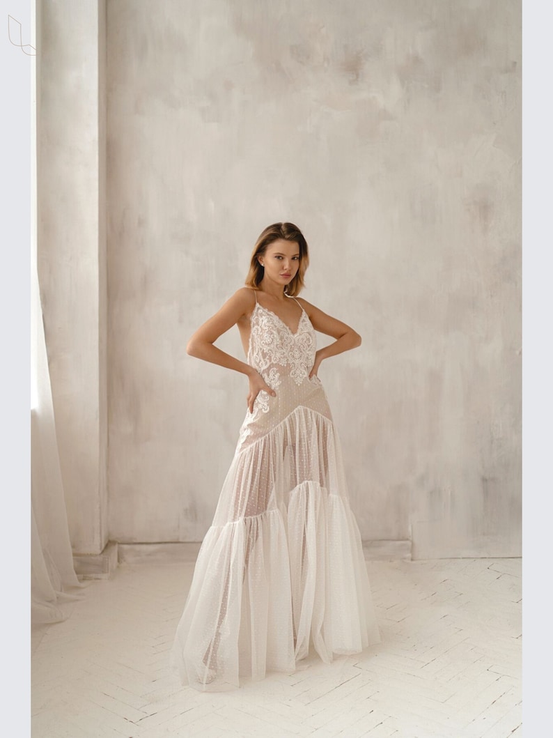 May include: A white, sheer, floor-length dress with lace detailing and a ruffled skirt.
