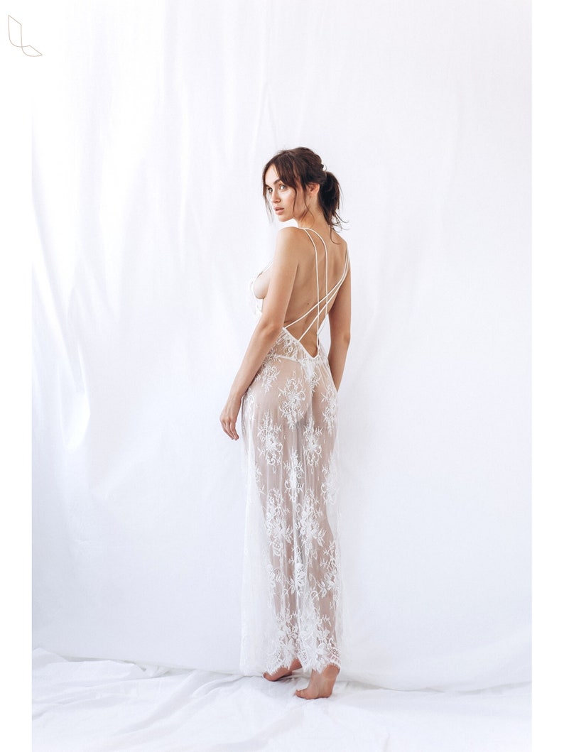 Puede incluir: Un vestido maxi de encaje blanco con espalda baja y tirantes finos. El vestido es transparente y tiene un delicado estampado floral.