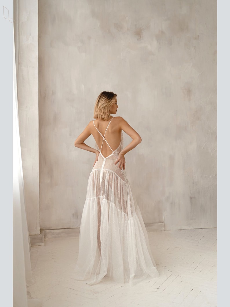 May include: A white, sheer, long, sleeveless dress with a criss-cross back detail and a tiered skirt.